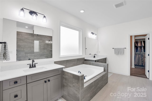 bathroom featuring two vanities, a bath, visible vents, and a sink