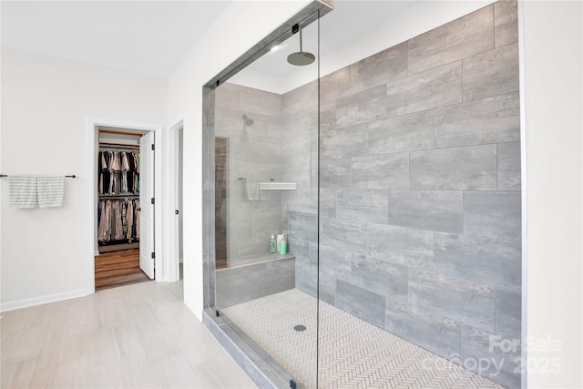 bathroom with a walk in closet, a shower stall, and baseboards