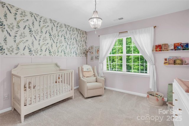 bedroom with a crib, visible vents, an inviting chandelier, and carpet flooring