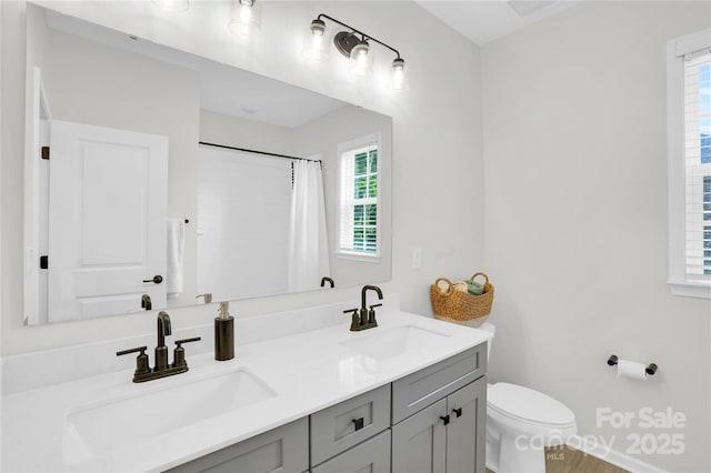 full bath with curtained shower, double vanity, toilet, and a sink