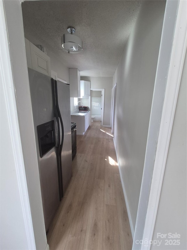 hall featuring baseboards, a textured ceiling, a sink, and light wood-type flooring