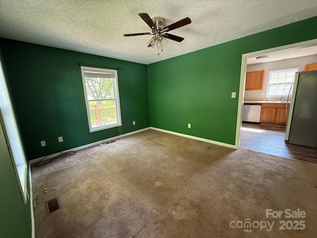 carpeted empty room with a textured ceiling, a ceiling fan, baseboards, and a sink