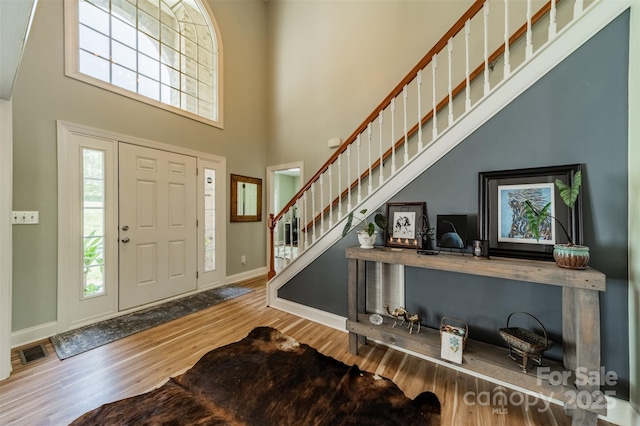 foyer entrance featuring stairway, wood finished floors, baseboards, a high ceiling, and visible vents
