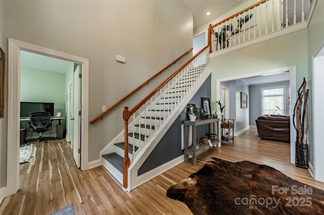 stairs featuring baseboards, wood finished floors, and a high ceiling