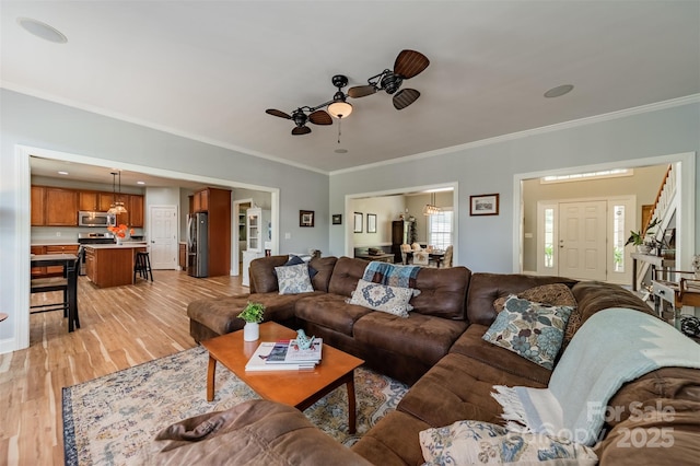 living room with light wood finished floors, crown molding, and ceiling fan
