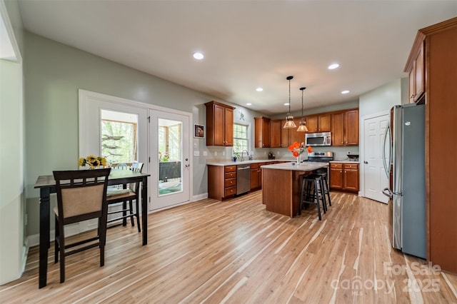kitchen featuring brown cabinets, a kitchen breakfast bar, a center island, light wood-style flooring, and appliances with stainless steel finishes