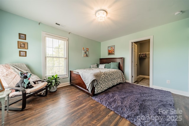 bedroom with a spacious closet, baseboards, wood finished floors, and visible vents