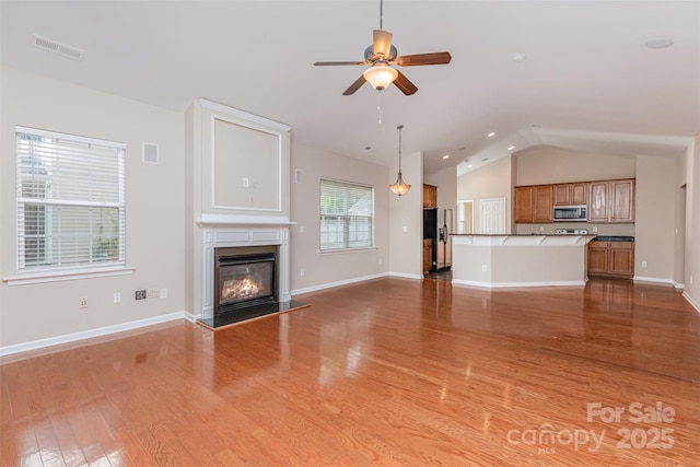 unfurnished living room with lofted ceiling, wood finished floors, visible vents, a ceiling fan, and a glass covered fireplace