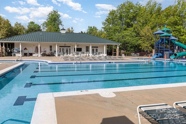 community pool with playground community, a water slide, french doors, and a patio