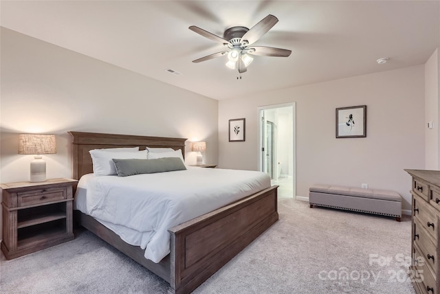 bedroom with a ceiling fan, visible vents, light colored carpet, baseboards, and ensuite bath