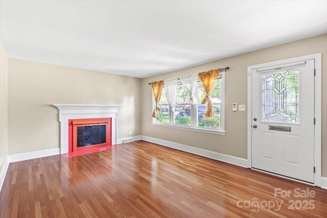 unfurnished living room with a fireplace with flush hearth, baseboards, a healthy amount of sunlight, and wood finished floors