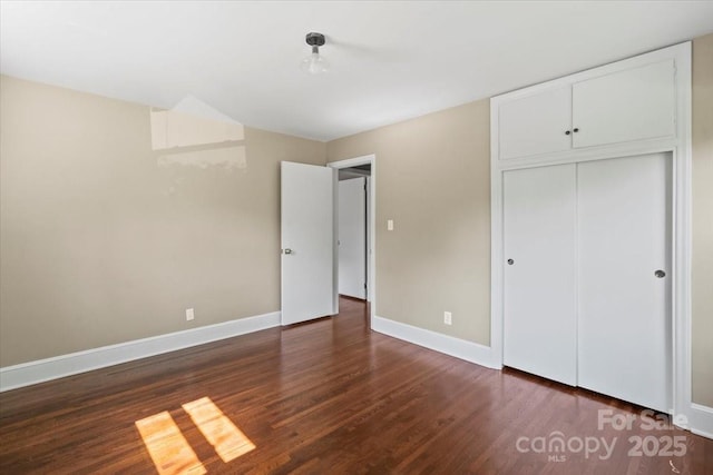 unfurnished bedroom featuring baseboards, wood finished floors, and a closet