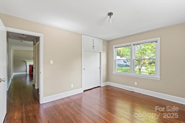 unfurnished bedroom featuring baseboards, visible vents, dark wood-style floors, and a closet