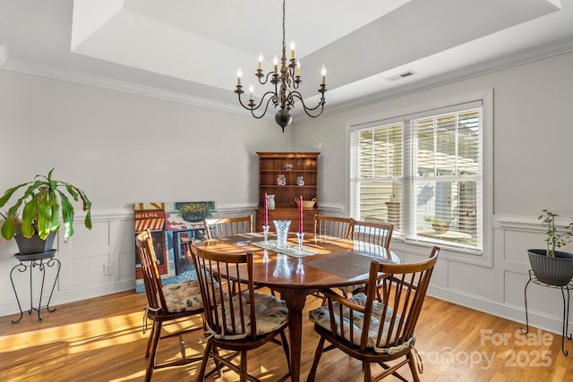 dining room with light wood-style flooring, a chandelier, a decorative wall, wainscoting, and crown molding