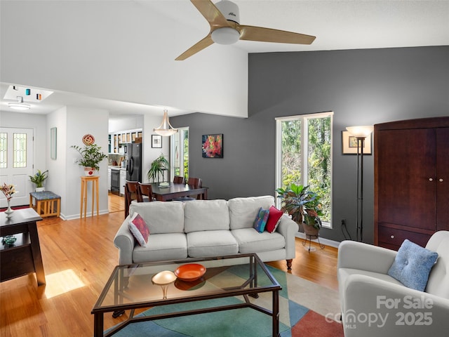 living area with high vaulted ceiling, light wood-style flooring, baseboards, and ceiling fan