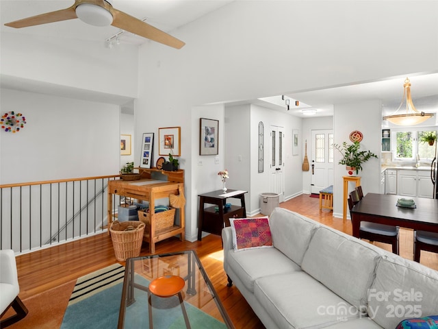 living area featuring track lighting, a towering ceiling, a ceiling fan, and wood finished floors