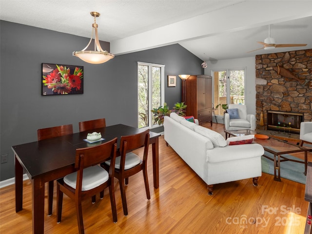 dining space featuring a stone fireplace, light wood-style flooring, ceiling fan, and lofted ceiling