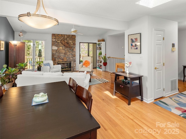 dining space with light wood finished floors, a stone fireplace, visible vents, and plenty of natural light