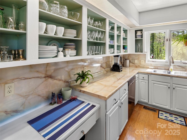 interior space with light wood-style flooring, backsplash, visible vents, stainless steel dishwasher, and a sink