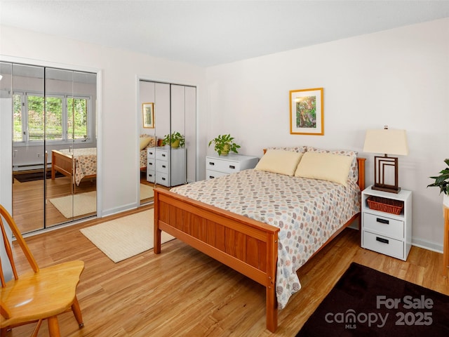 bedroom featuring baseboard heating, light wood-style floors, baseboards, and multiple closets