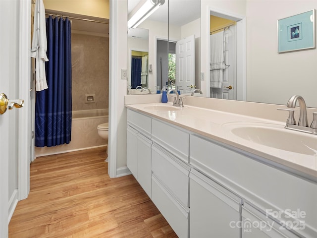 full bath featuring a sink, toilet, double vanity, and wood finished floors