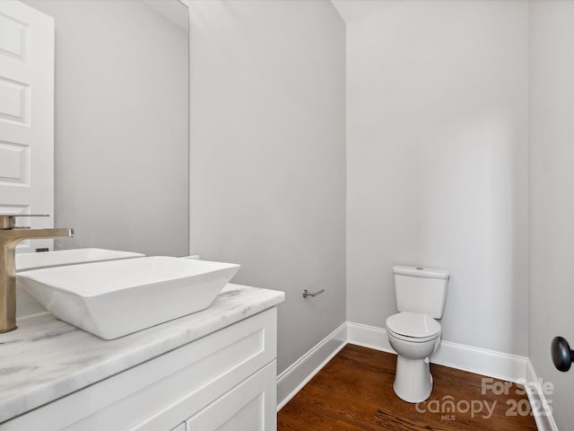 half bath featuring toilet, wood finished floors, vanity, and baseboards