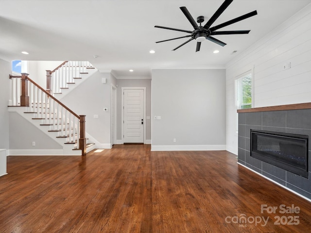 unfurnished living room with ceiling fan, ornamental molding, stairway, wood finished floors, and a tiled fireplace