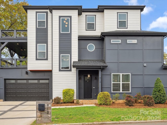 view of front of house featuring an attached garage, a shingled roof, a front yard, and driveway