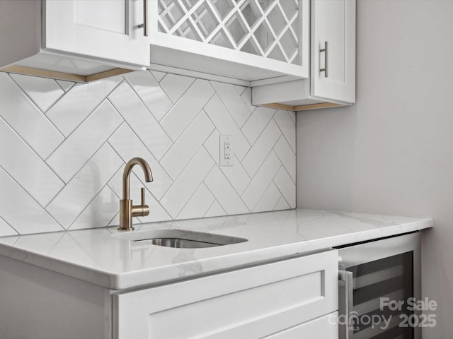 kitchen featuring light stone counters, white cabinetry, decorative backsplash, beverage cooler, and a sink