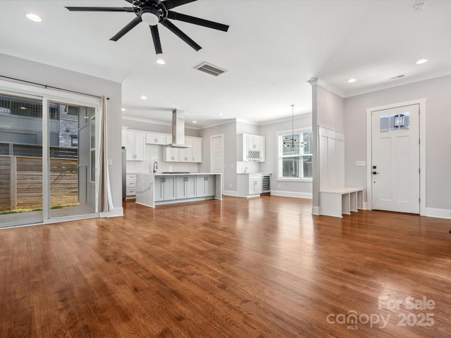unfurnished living room with ceiling fan with notable chandelier, ornamental molding, visible vents, and recessed lighting