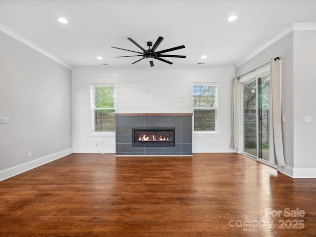 unfurnished living room featuring wood finished floors, a tiled fireplace, ornamental molding, and recessed lighting
