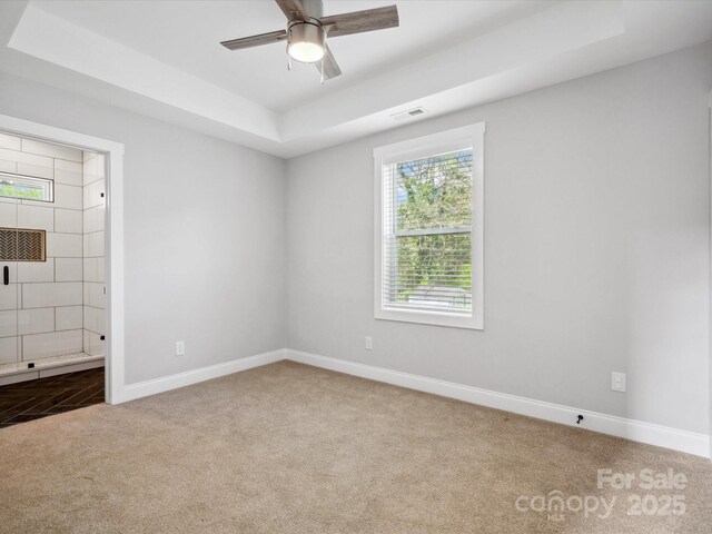 carpeted spare room with visible vents, baseboards, a raised ceiling, and a ceiling fan