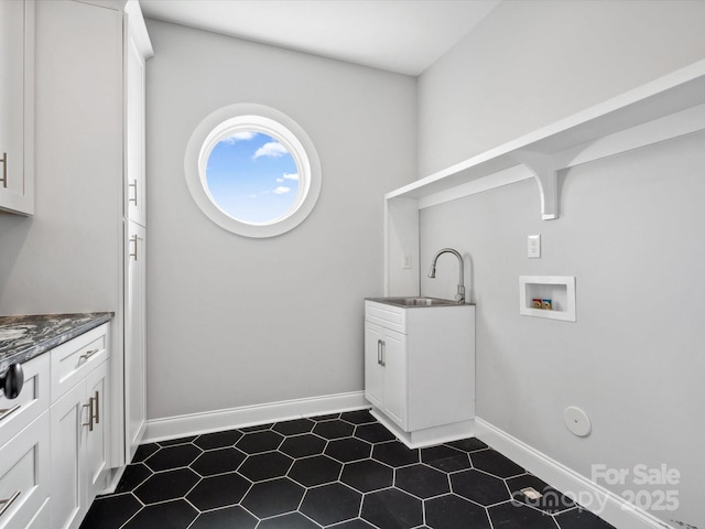 laundry area featuring baseboards, hookup for a washing machine, cabinet space, a sink, and dark tile patterned flooring