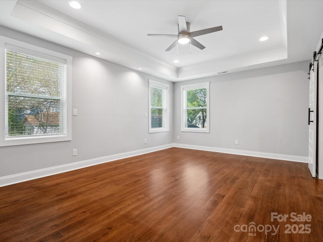 unfurnished room with ceiling fan, recessed lighting, a barn door, a raised ceiling, and dark wood-style floors