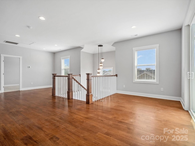 empty room with wood finished floors, attic access, baseboards, and visible vents