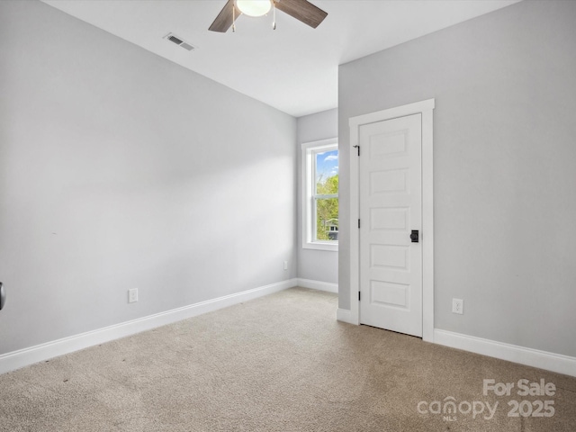 carpeted spare room featuring baseboards, a ceiling fan, and visible vents