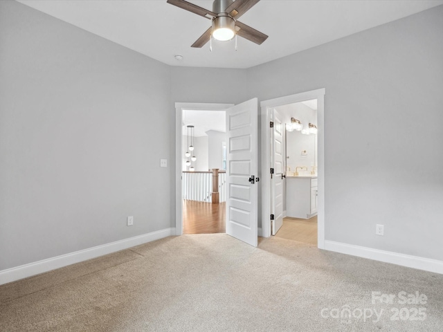 unfurnished bedroom featuring light carpet, ensuite bath, baseboards, and ceiling fan