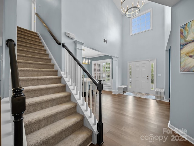 foyer featuring visible vents, a chandelier, stairway, wood finished floors, and a towering ceiling