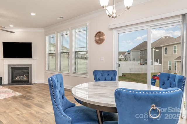 dining room featuring visible vents, baseboards, ornamental molding, wood finished floors, and a glass covered fireplace