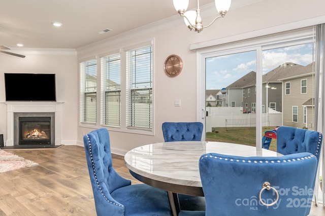 dining room with a glass covered fireplace, baseboards, ornamental molding, visible vents, and wood finished floors