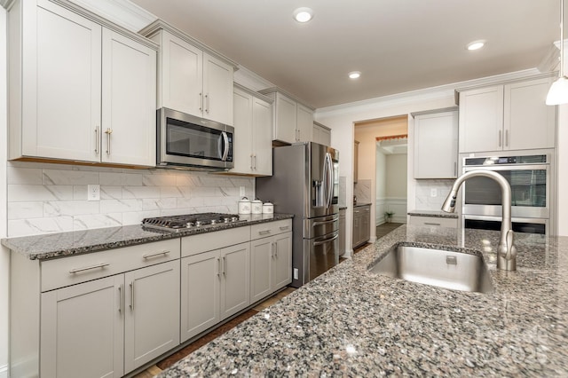 kitchen with a sink, ornamental molding, dark stone countertops, and stainless steel appliances