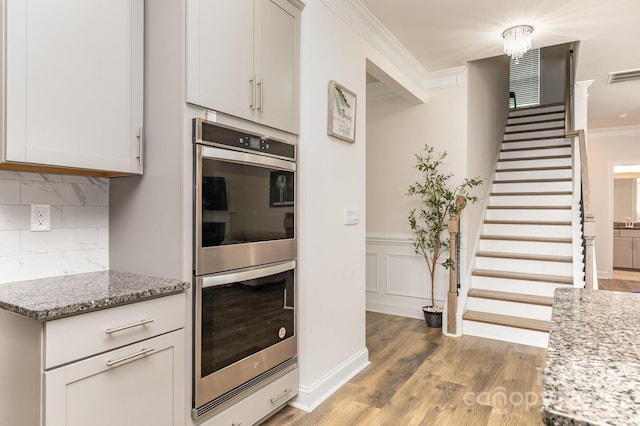 kitchen with crown molding, light wood-style floors, visible vents, decorative backsplash, and double oven
