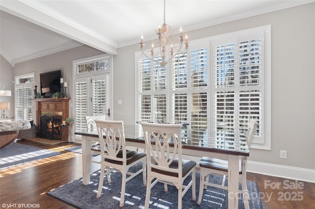 dining area with baseboards, a warm lit fireplace, a chandelier, crown molding, and wood finished floors