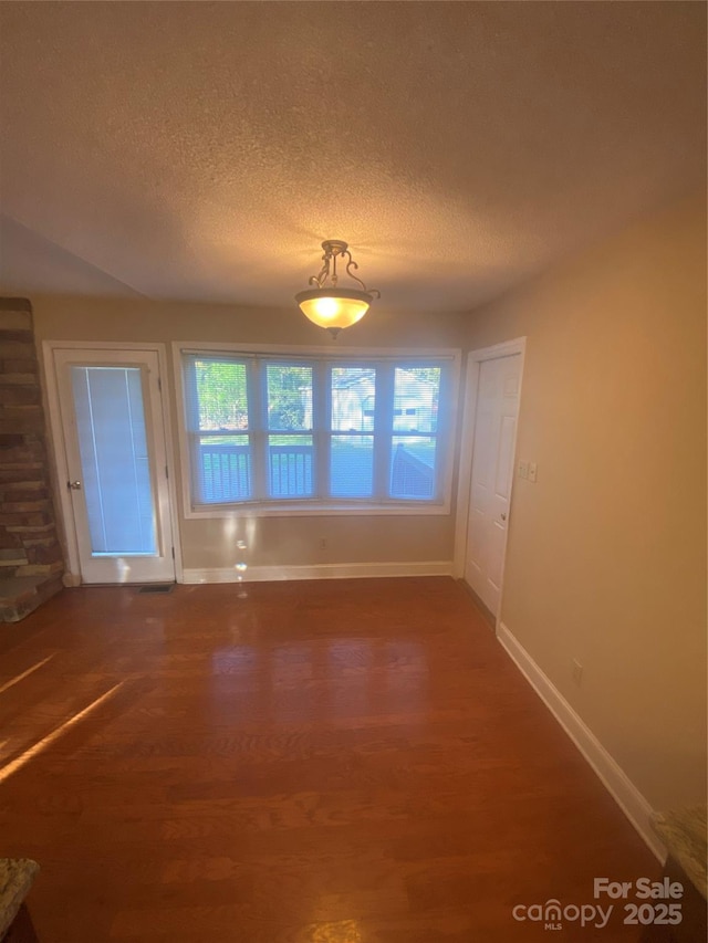 unfurnished dining area with a textured ceiling, wood finished floors, and baseboards