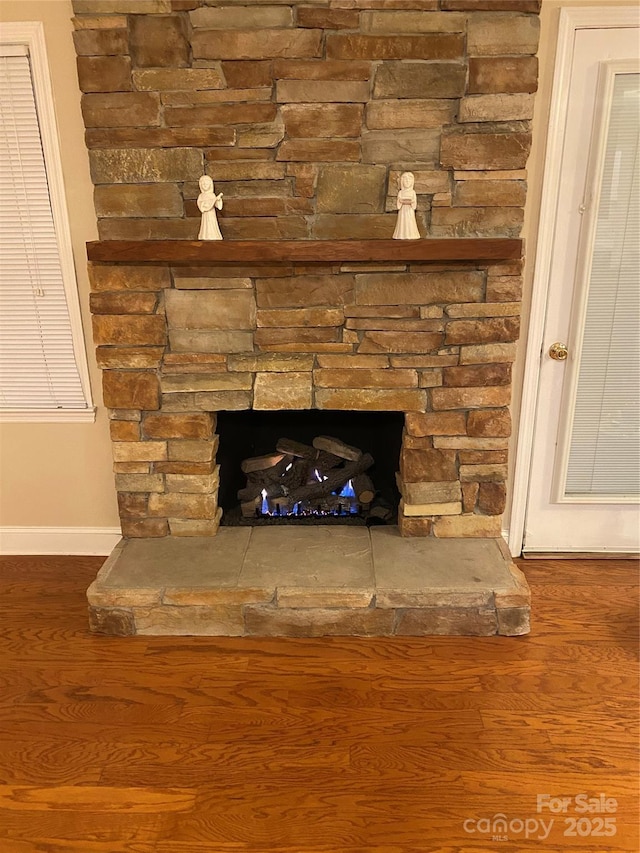 interior details featuring a stone fireplace, baseboards, and wood finished floors