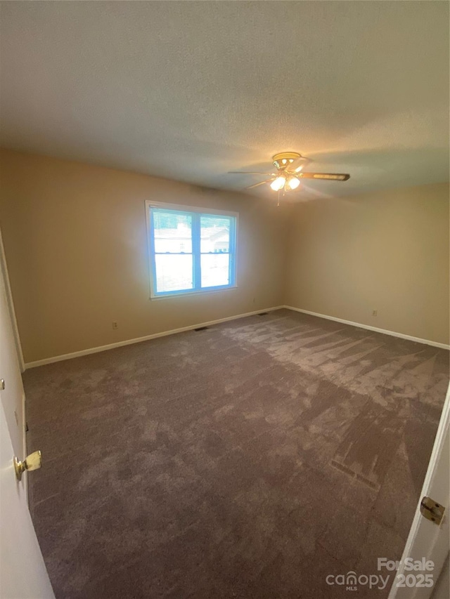empty room featuring dark colored carpet, baseboards, a ceiling fan, and a textured ceiling