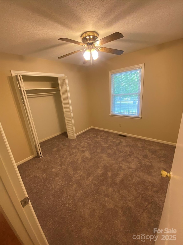 unfurnished bedroom featuring dark carpet, a textured ceiling, a closet, and ceiling fan