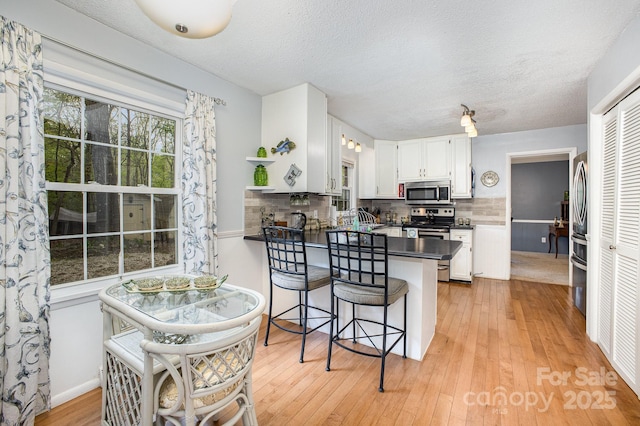 147 Spring Shore Rd, Statesville, NC 28677 - kitchen with white cabinets, dark countertops, light wood-type flooring, appliances with stainless steel finishes, and a peninsula