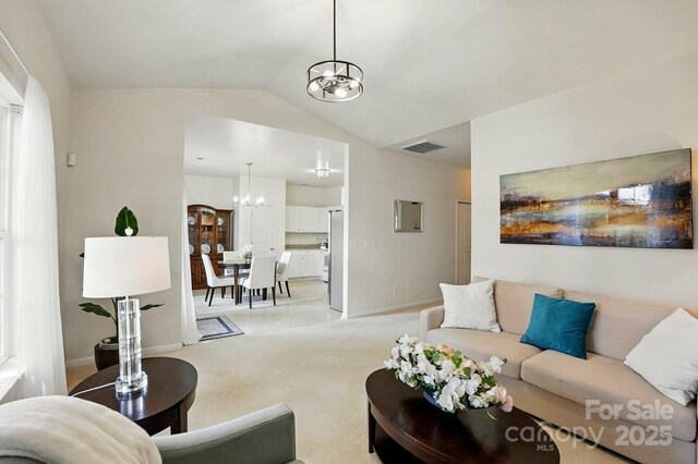 living area with visible vents, lofted ceiling, light carpet, baseboards, and a notable chandelier