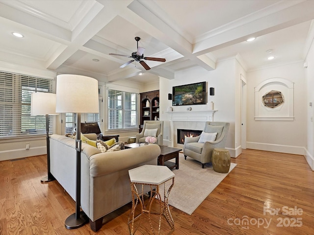 living area with a ceiling fan, coffered ceiling, light wood-type flooring, baseboards, and a glass covered fireplace